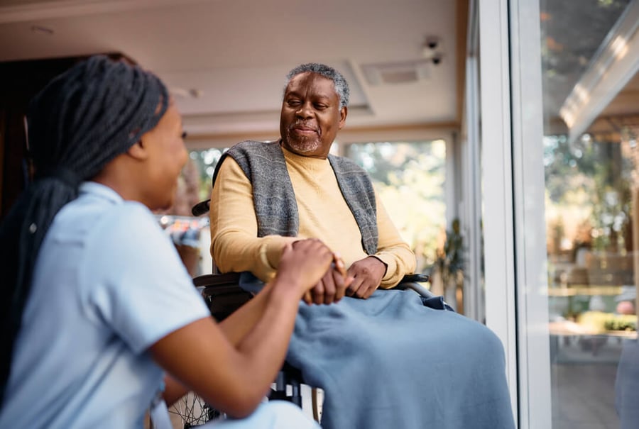 Caregiver compassionately holding hands with an elderly man in a wheelchair at a care facility