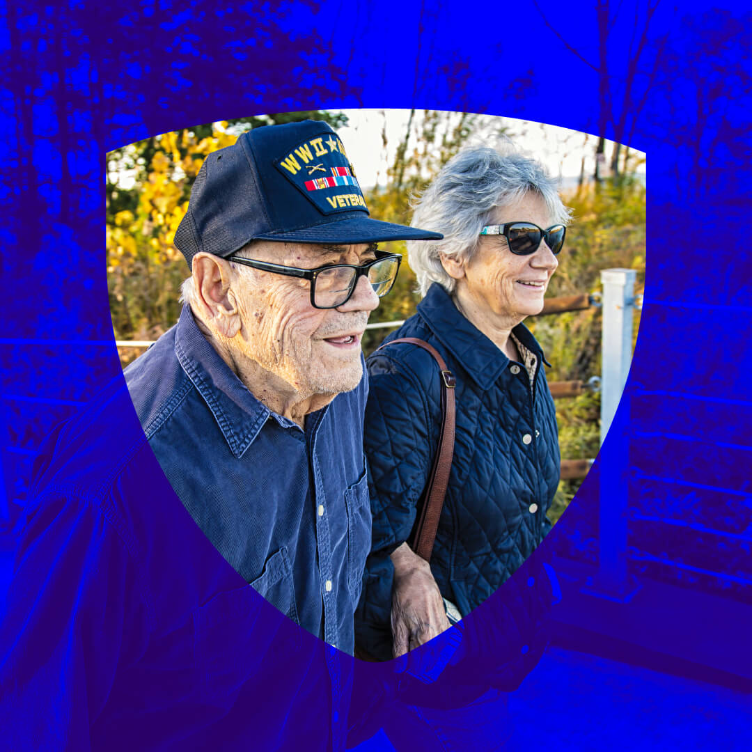 Elderly Veteran wearing military cap with service ribbons standing outdoors with senior woman in quilted jacket, both smiling in autumn setting with decorative blue border Elderly Veteran wearing military cap with service ribbons standing outdoors with senior woman in quilted jacket, both smiling in autumn setting with decorative blue border