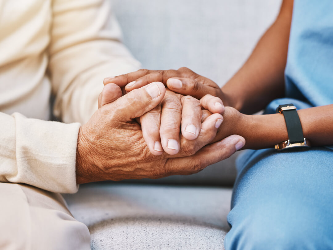 Close-up of younger hands gently holding elderly hands in a caring, supportive gesture