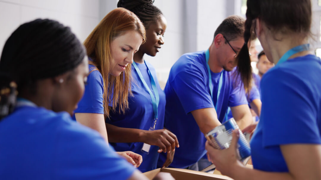 Diverse group of volunteers in matching blue shirts working together to pack items into boxes, engaged in community service or charitable activity. Diverse group of volunteers in matching blue shirts working together to pack items into boxes, engaged in community service or charitable activity.